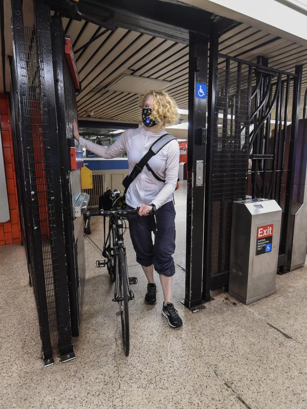 A woman wheels a bike goes through the service gate near subway turnstiles.